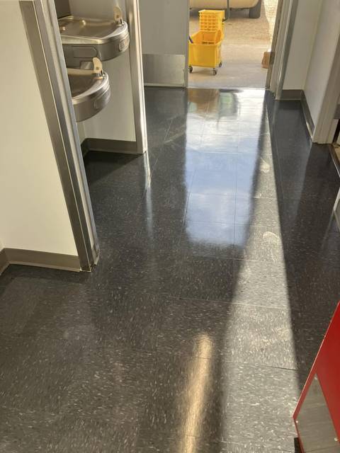 A dark speckled floor and a mop bucket at the end of the hall