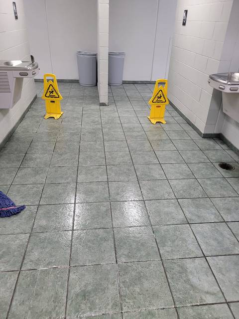 A restroom floor still wet, with yellow wet-floor signs out